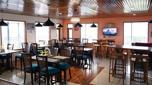 A restaurant with multiple dining areas, including a bar and booths. There are ceiling fans and pendant lights. - Orchard Green Shimla (Shimla)