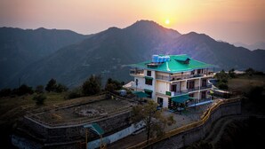 A two-story building with a green roof, located in a mountainous area with a sunset in the background. - Orchard Green Shimla (Shimla)