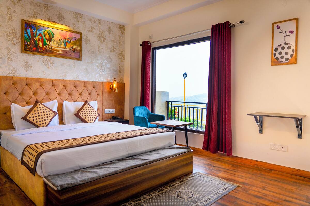 A hotel room with a large bed, a view of the outdoors, a small table, and a chair.