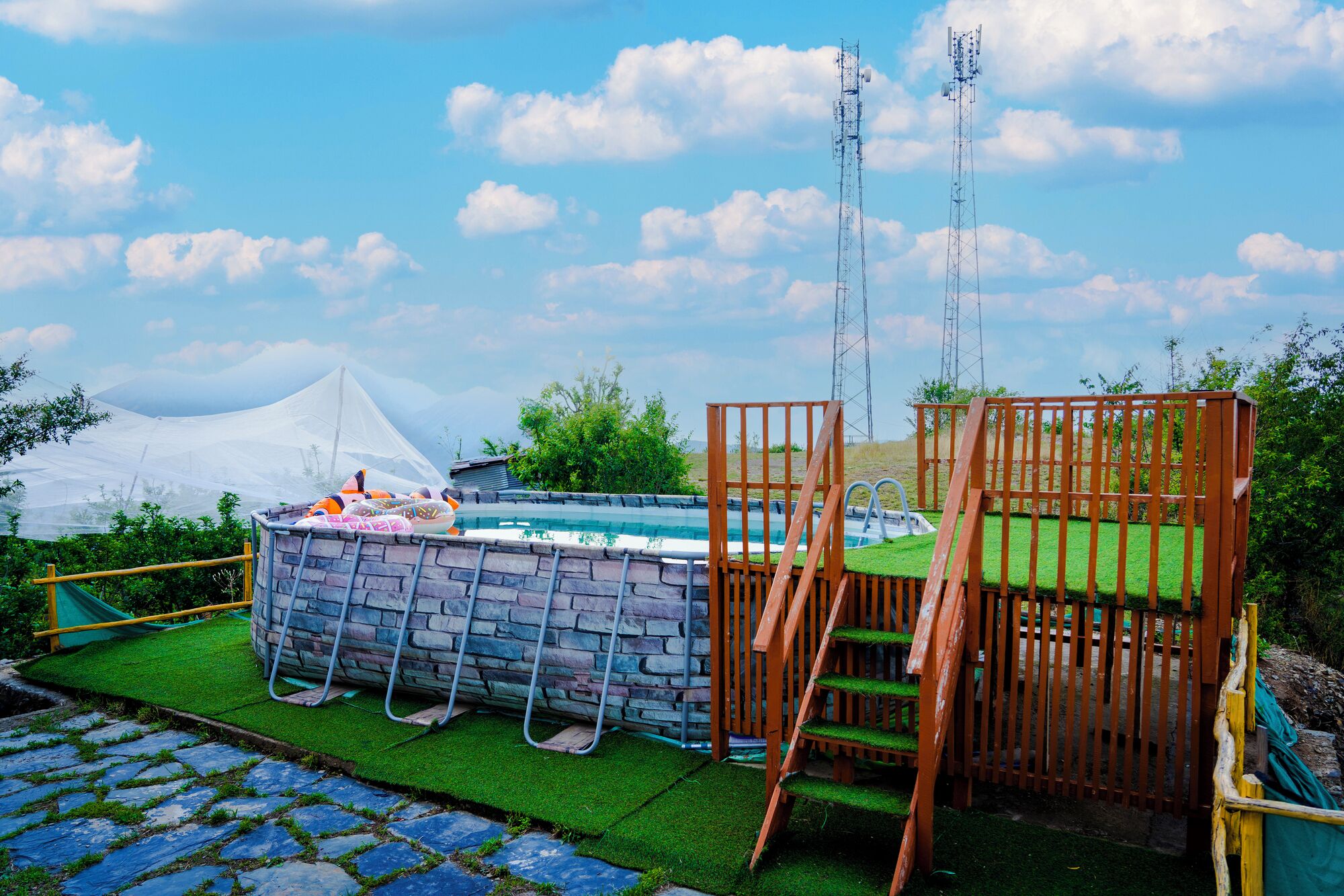 An outdoor swimming pool with a stone wall, surrounded by a wooden fence and a green artificial turf area.