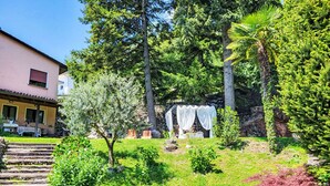 A garden with a stone wall, a wooden staircase, and a building with a yellow facade. - Ca`Sotselva by Interhome (Besazio)