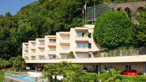 A multi-story hotel with balconies, a swimming pool, and lush greenery.