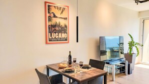 A dining area with a table set for two, a bottle of wine, and a poster on the wall.
