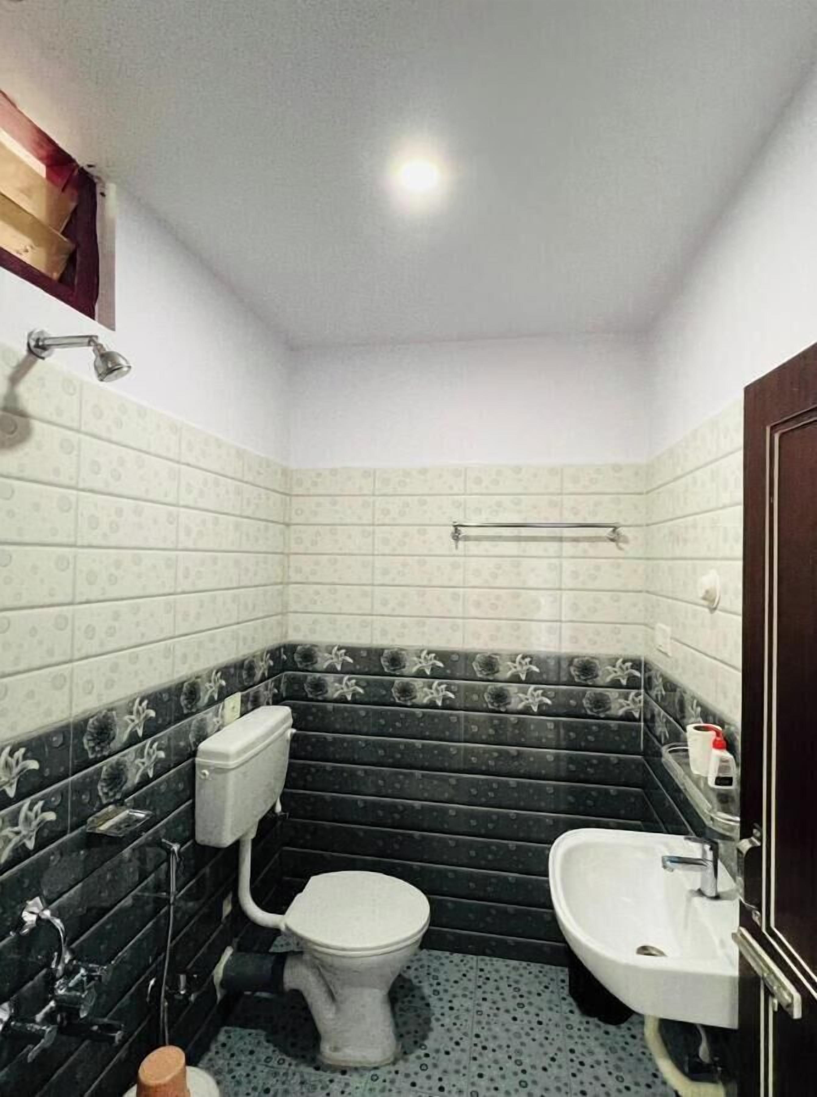 Un baño pequeño y funcional con inodoro, bidé y lavamanos. Las paredes están cubiertas de azulejos con un diseño y hay un cabezal de ducha en la pared.