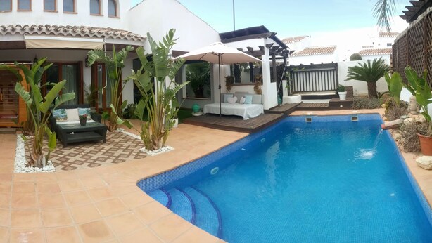 A swimming pool with a tiled edge, surrounded by a patio area with a checkered floor pattern, a wooden deck, and a covered seating area with a white canopy. - Lux Villa LONG-TERM RENT for 7 ppl, Private pool, Sauna, Tennis, Gym, Golf, swim (Baños y Mendigo)