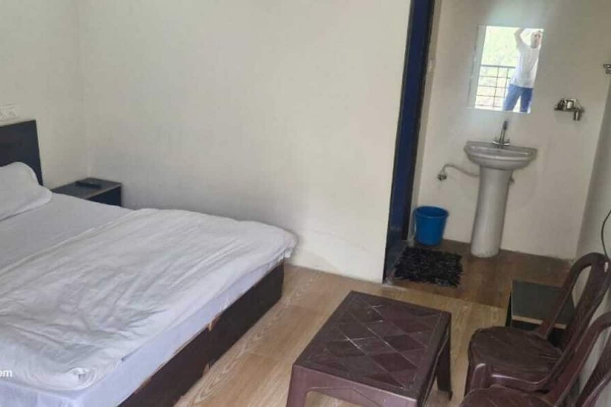A bedroom with a bed, a nightstand, a small table, a chair, a sink, and a window.
