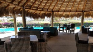 An outdoor seating area with wicker furniture and a thatched roof. - Contemporary Conveniently Located 1 BR condo, Walk to beach, restaurants & bars. (San José del Cabo)
