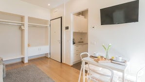A modern, well-lit room with a wooden floor, a white dining table with chairs, a flat-screen TV mounted on the wall, and a kitchenette area. - MT Studio by Rent All Como by Rent all Como (Como)