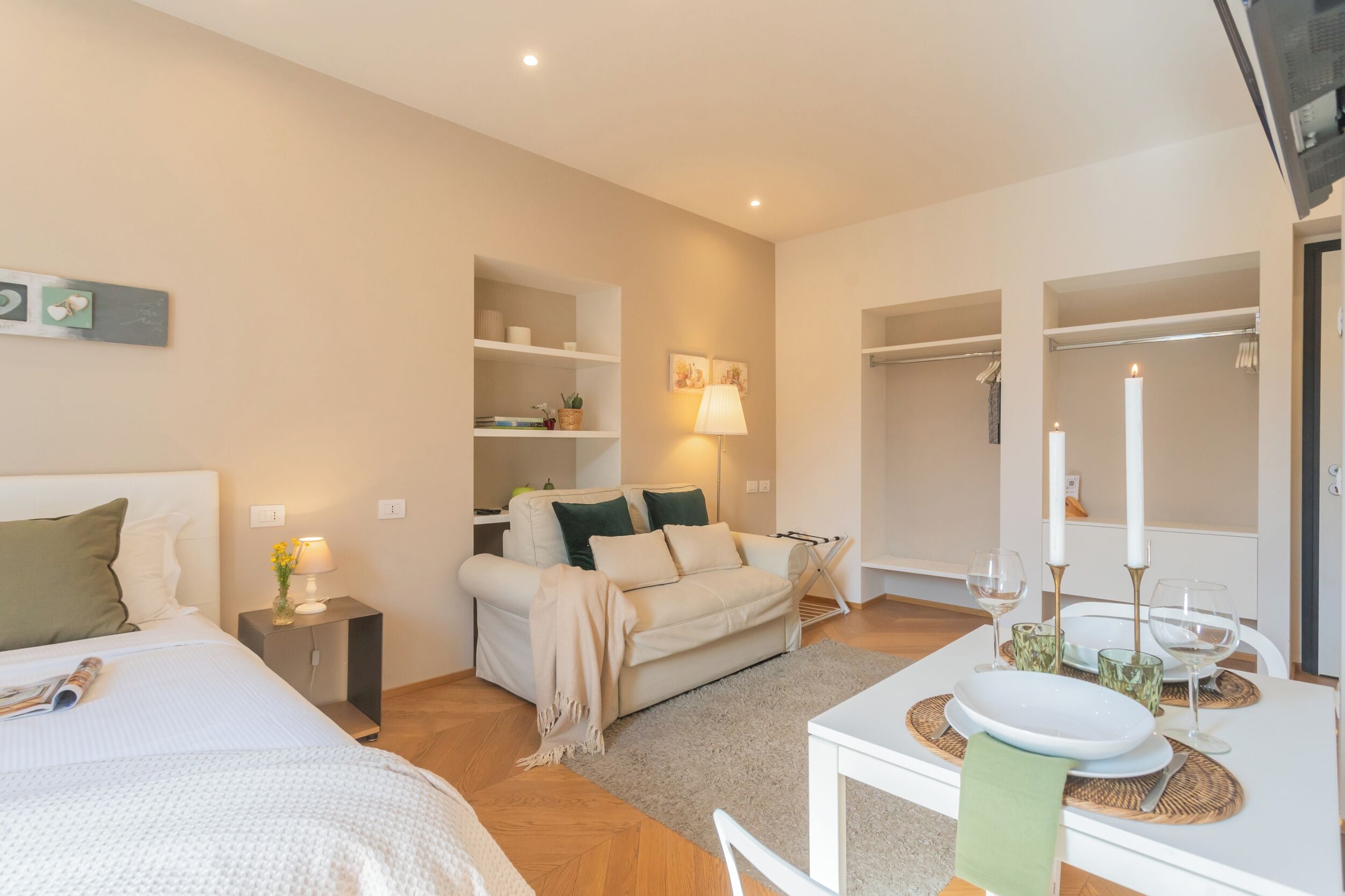 Une chambre d’hôtel moderne comprenant un lit, un canapé, une table à manger avec une bougie et une armoire.