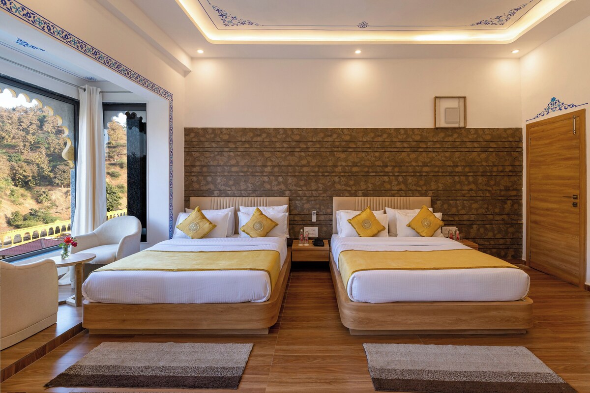 A double room with two beds, a wooden floor, a view of a mountainous landscape, and a ceiling with a decorative pattern.