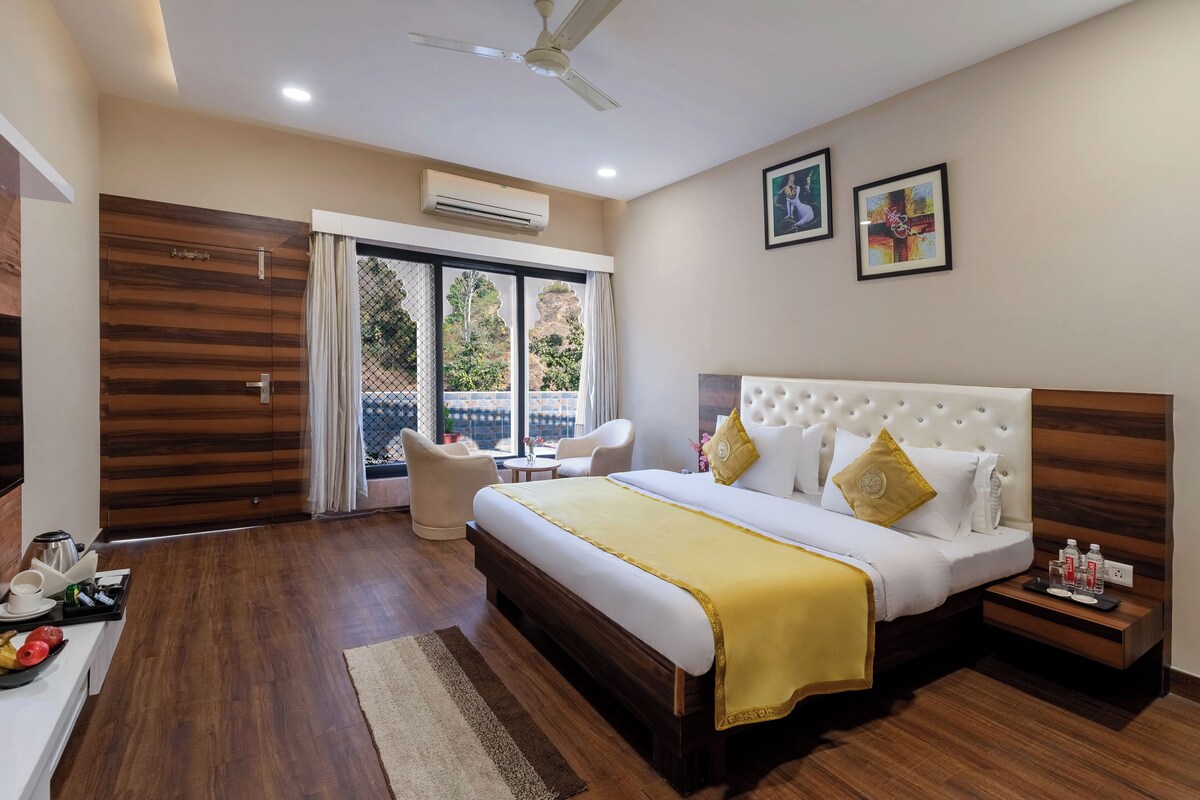 A hotel room with a large bed, a bedside table, a chair, a desk with a coffee maker, and a view through a sliding door.