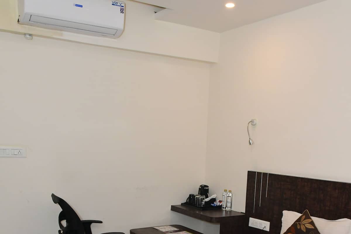 Quarto de hotel com cama, escrivaninha, cadeira, mesa pequena e ar condicionado.