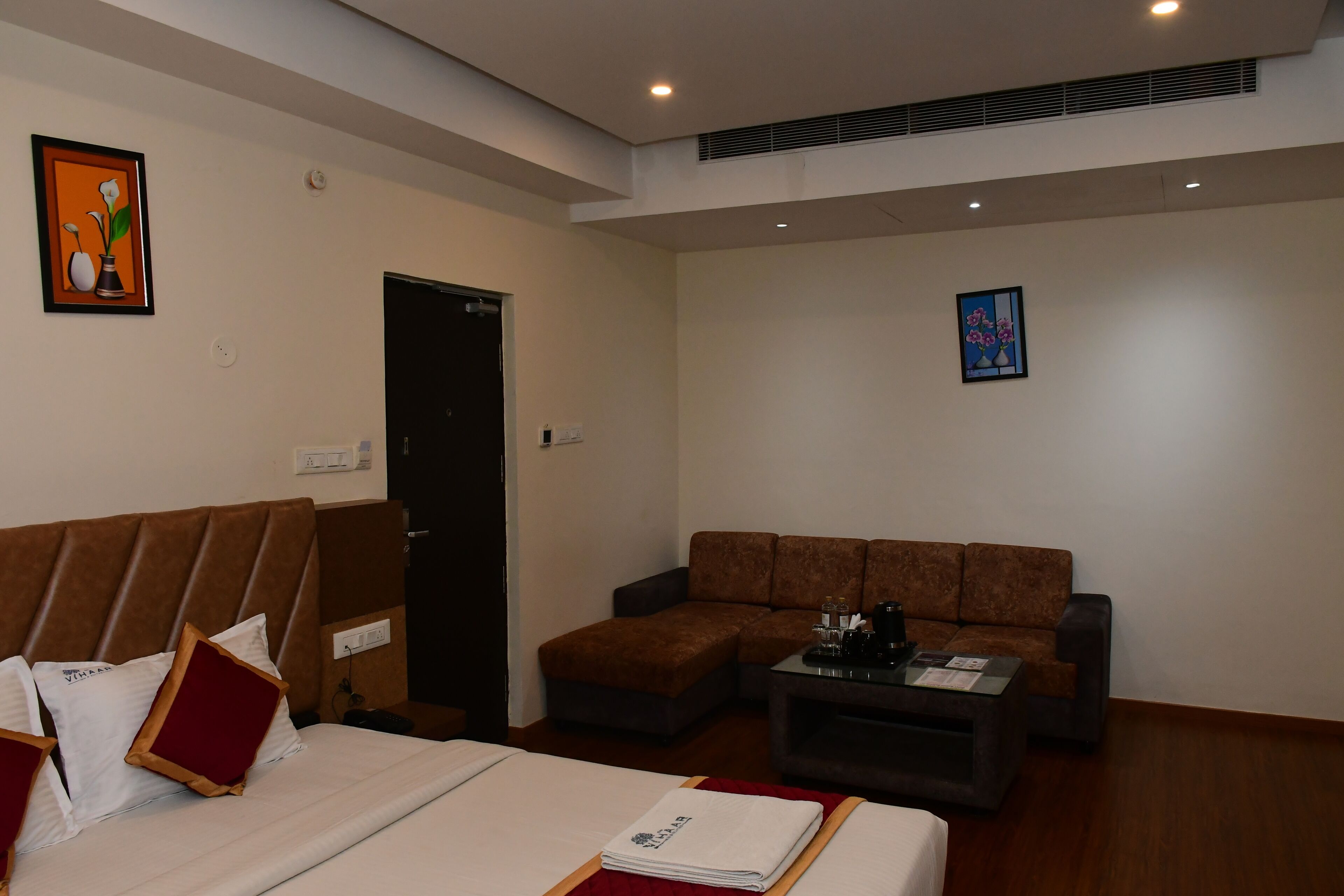 A hotel room with a bed, a sofa, a coffee table, and two paintings on the walls.