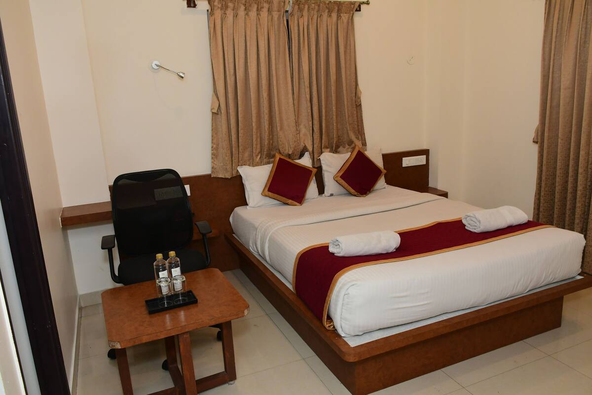 Quarto de hotel com uma cama, uma escrivaninha, uma cadeira e uma mala.