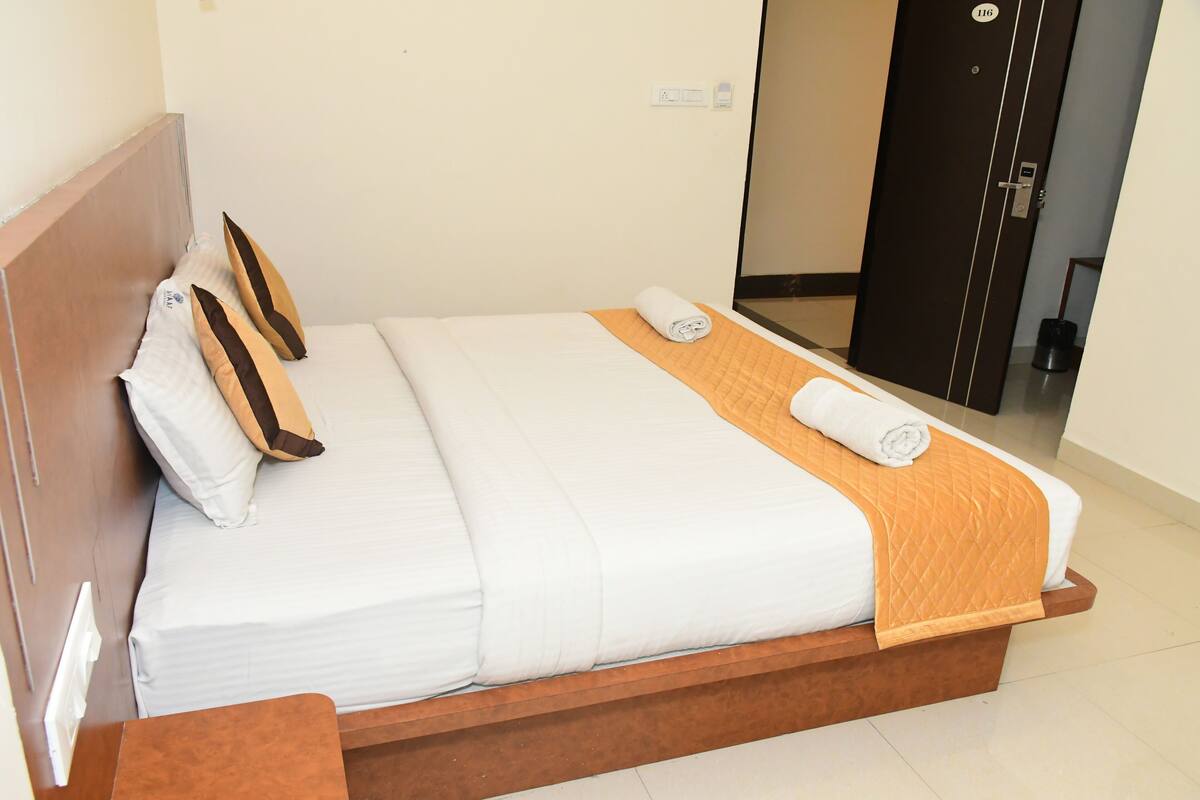 Uma cama bem arrumada com lençóis brancos e almofadas castanhas, uma cabeceira de madeira e uma mesinha de cabeceira castanha.