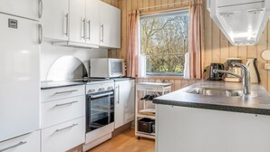Une cuisine de taille réduite avec des meubles blancs, un four à micro-ondes, un four traditionnel, un évier et une fenêtre avec des rideaux.