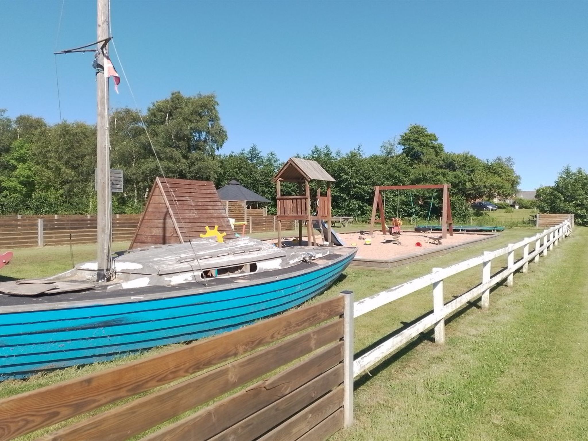 Un parque infantil con tobogán, columpios y una pequeña estructura de madera.