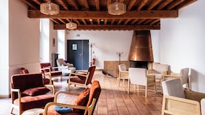 A spacious lobby with wooden beams, a large fireplace, and multiple seating areas with chairs and sofas. - Hostel Coeur de Cité (Carcassonne)