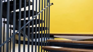 A staircase with wooden steps and black metal railings against a yellow wall. - Hostel Coeur de Cité (Carcassonne)