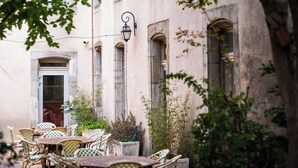 An outdoor seating area with wicker chairs and tables, a stone building with arched windows, and a hanging lantern. - Hostel Coeur de Cité (Carcassonne)