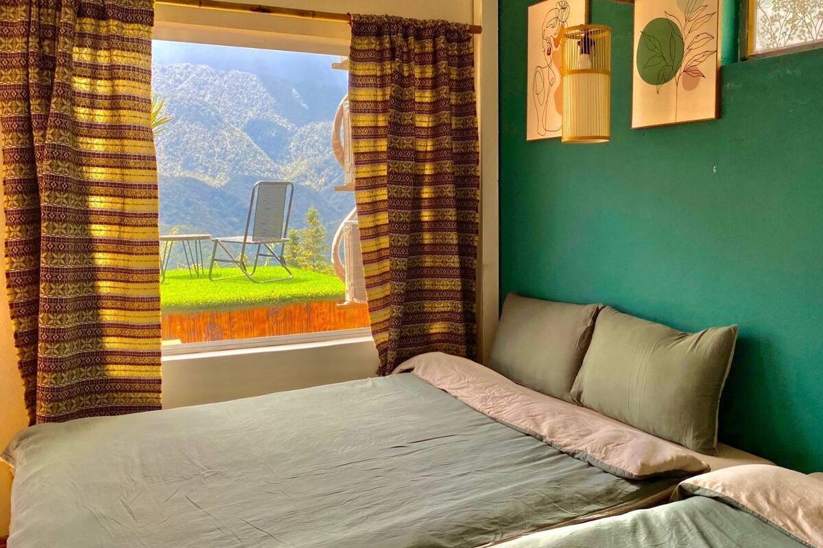 A bedroom with a bed, green walls, and a view of a mountain landscape through open curtains.