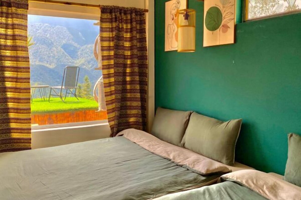 A bedroom with a bed, curtains, a view of mountains, and a chair outside the window.