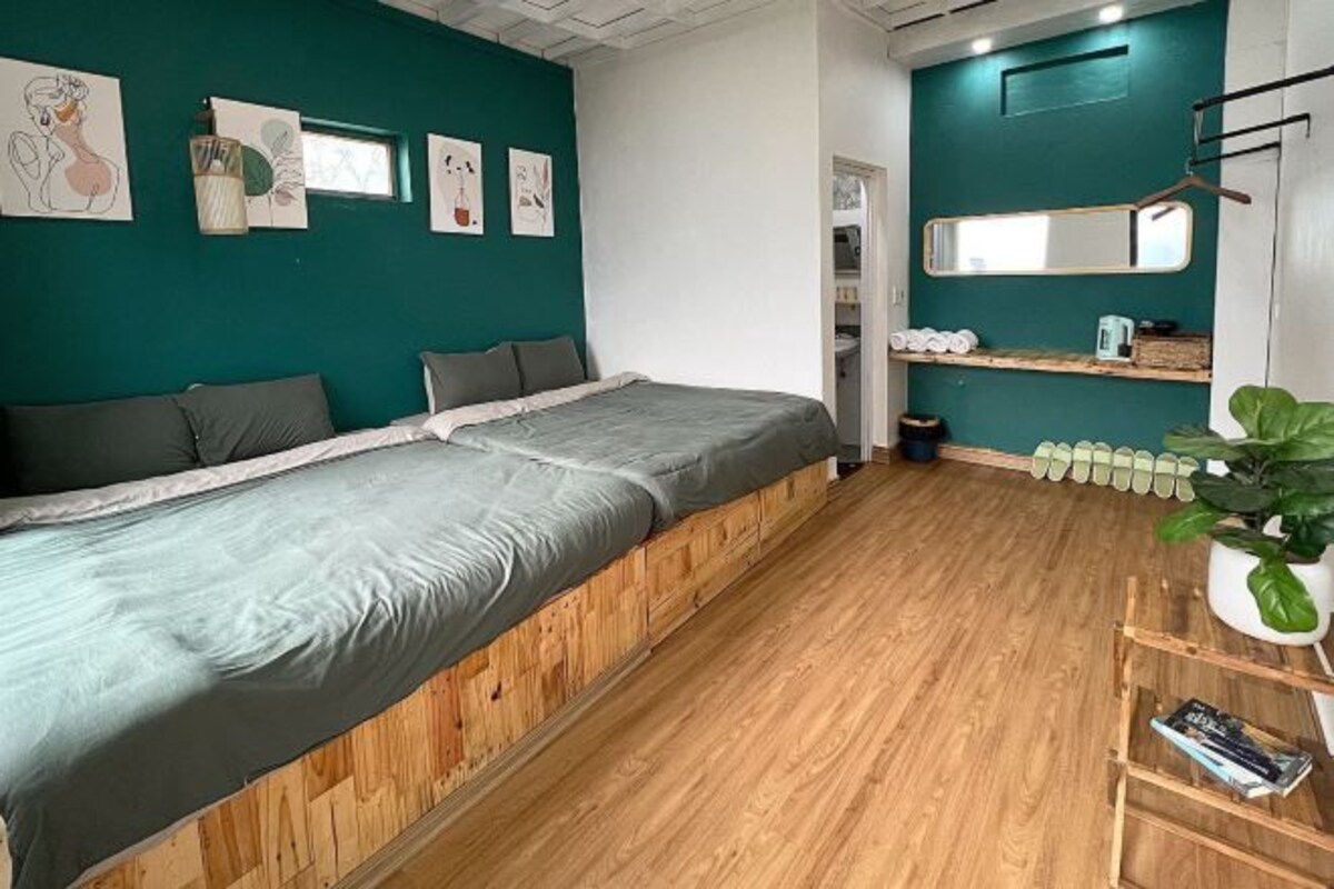 A bedroom with a large bed, wooden flooring, teal walls, and a small plant.