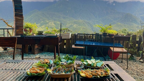An outdoor dining area with a view of mountains, wooden furniture, and a variety of dishes. - D Home Sapa 2 (Sa Pa)