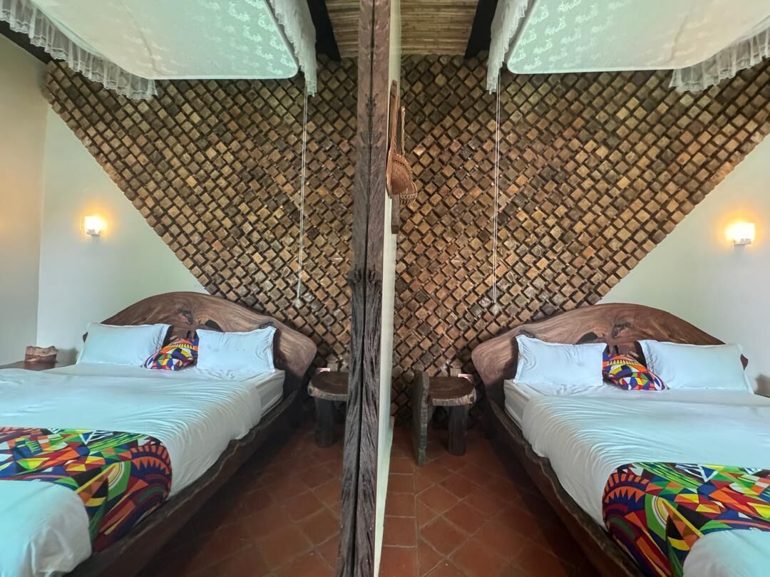 A room with two beds, a wooden ceiling, and a patterned wall.