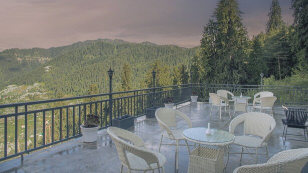 A terrace with wicker furniture, potted plants, and a view of a forested mountain range.