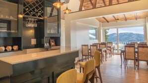A modern kitchen with a bar area, wooden ceiling beams, and large windows offering a mountain view.