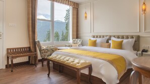 A bedroom with a large bed, a bench, a chair, and a view of mountains through a window.
