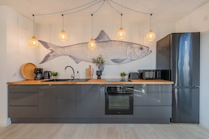 Una cocina moderna con un mural de peces, luces colgantes, un refrigerador de acero inoxidable y un horno empotrado.