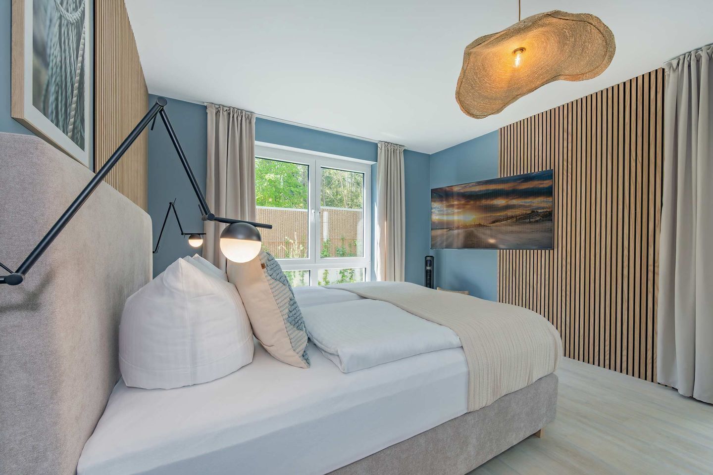 Een slaapkamer met een bed, een bureau, een stoel, een raam en een tv aan de muur.