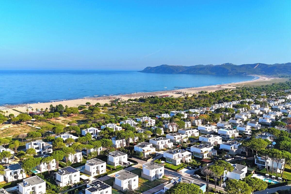 Uma área residencial costeira com fileiras de casas brancas, uma praia e um céu azul límpido.