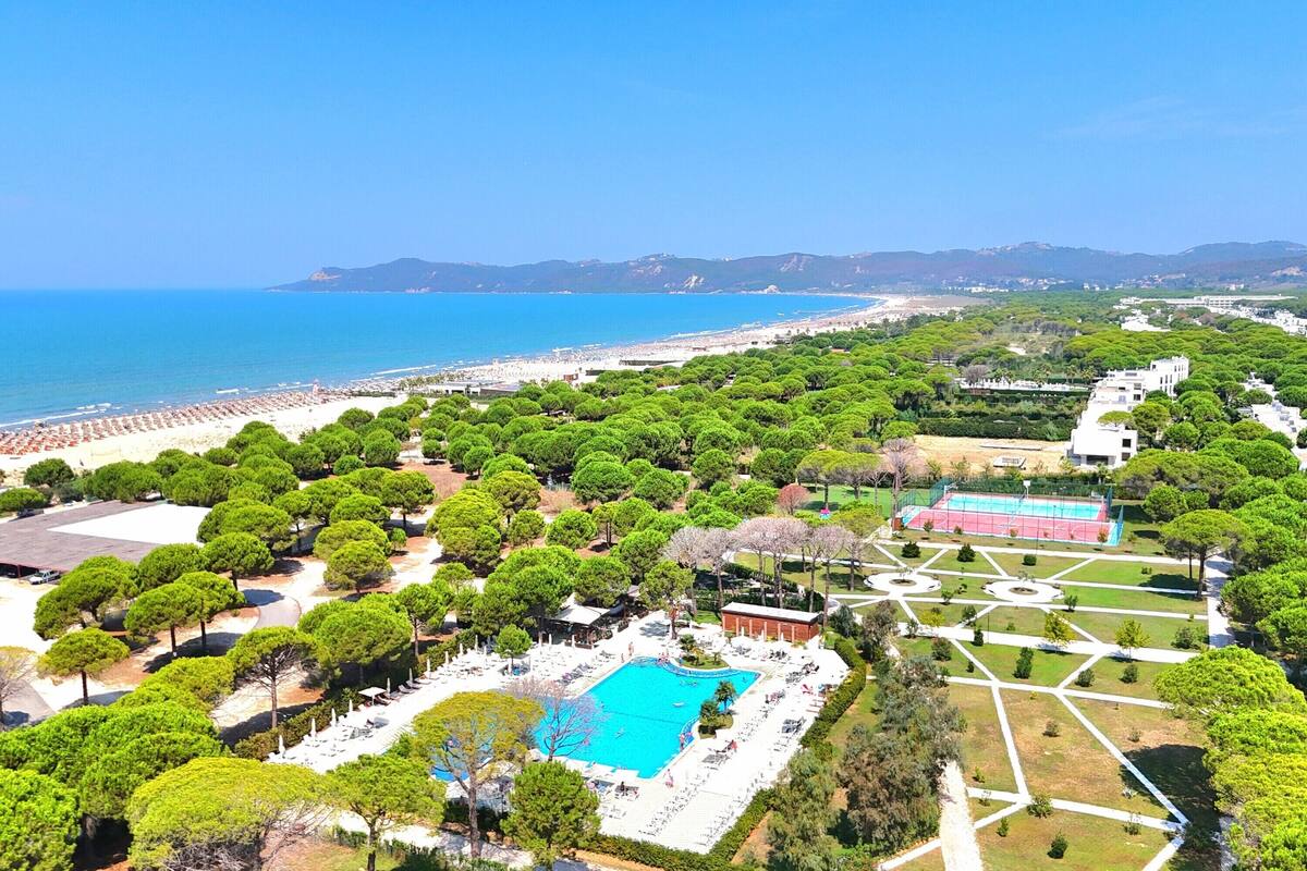 Vista aérea de um resort com piscina, praia e vegetação exuberante.