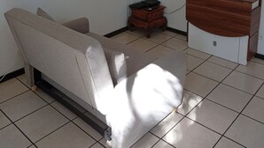 En stue med en sofa, et fjernsyn ophængt på væggen, et lille træsidebord og en dekorativ vægdekoration.
