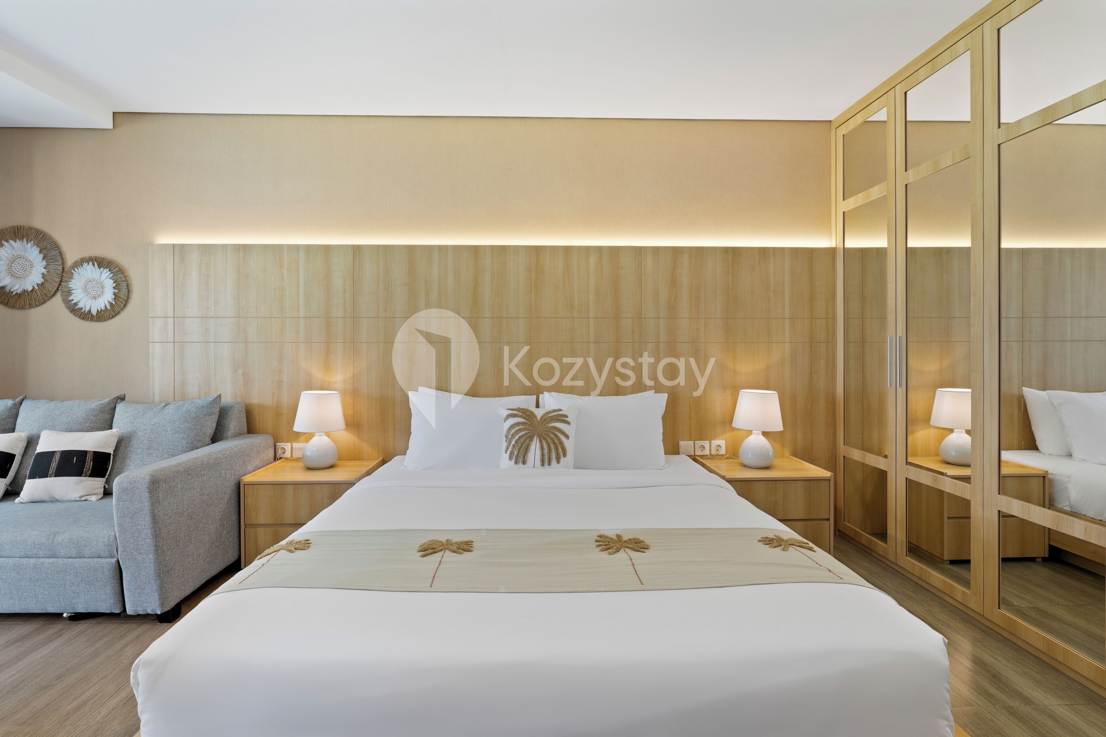 A hotel room with a large bed, two bedside tables with lamps, a sofa, and a wardrobe.