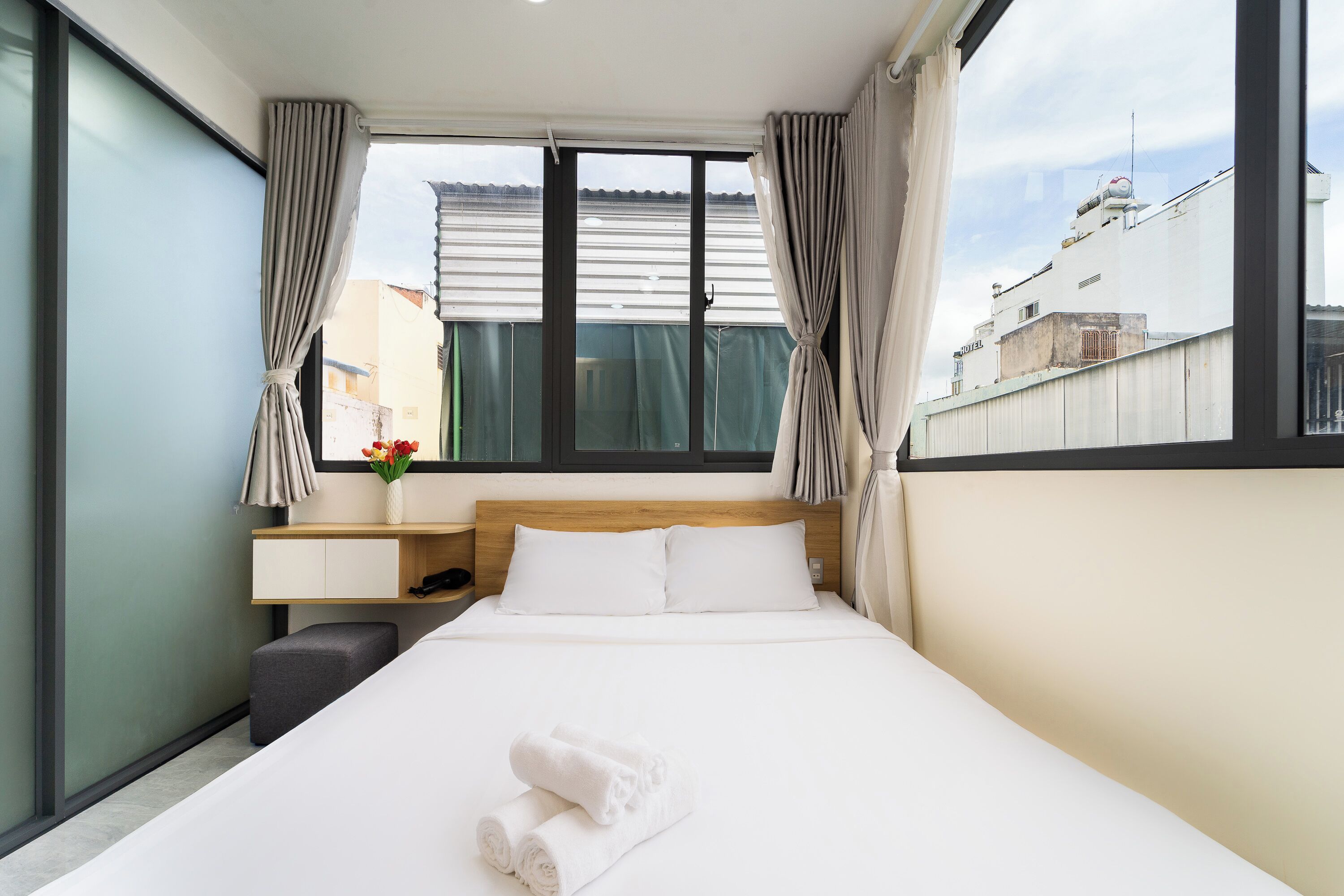 A hotel room with a large bed, a bedside table, a small desk, and a window with curtains.
