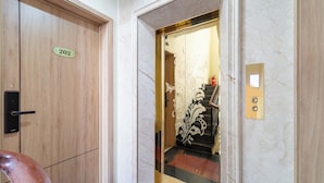 Ein Hotelzimmer-Eingang mit einer Holztür, auf der '202' steht, einer Marmorwand und einem modernen Aufzug mit floralem Dekor.