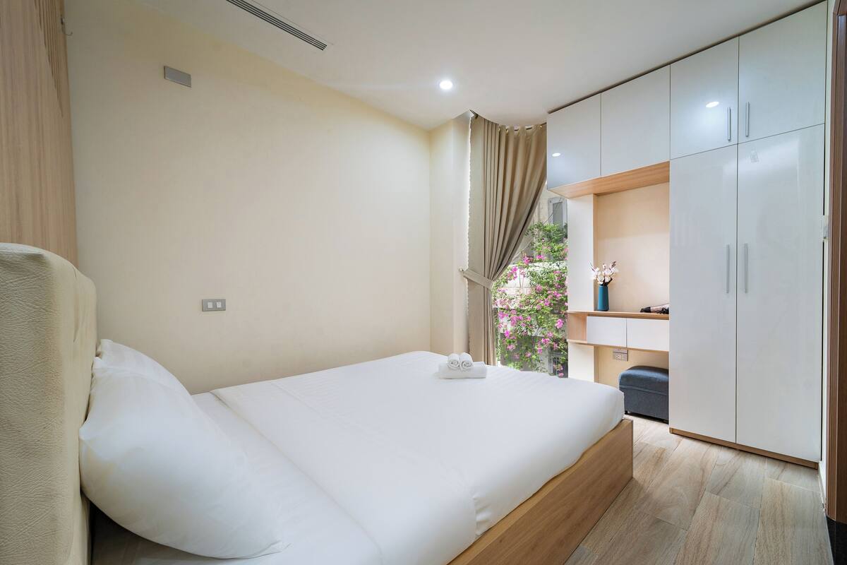 Une chambre à coucher avec un lit, une armoire, une fenêtre avec des rideaux et un petit balcon agrémenté de fleurs.