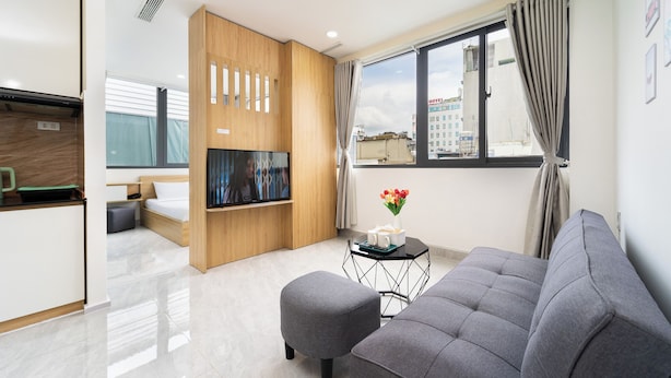 Ein modernes Hotelzimmer mit einer Couch, einem kleinen Tisch mit einer Vase, einem Fernseher und einer Küchenzeile.