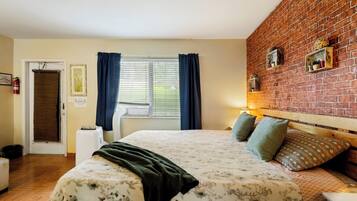 A bedroom with a bed, a brick wall, a window with curtains, and a door.