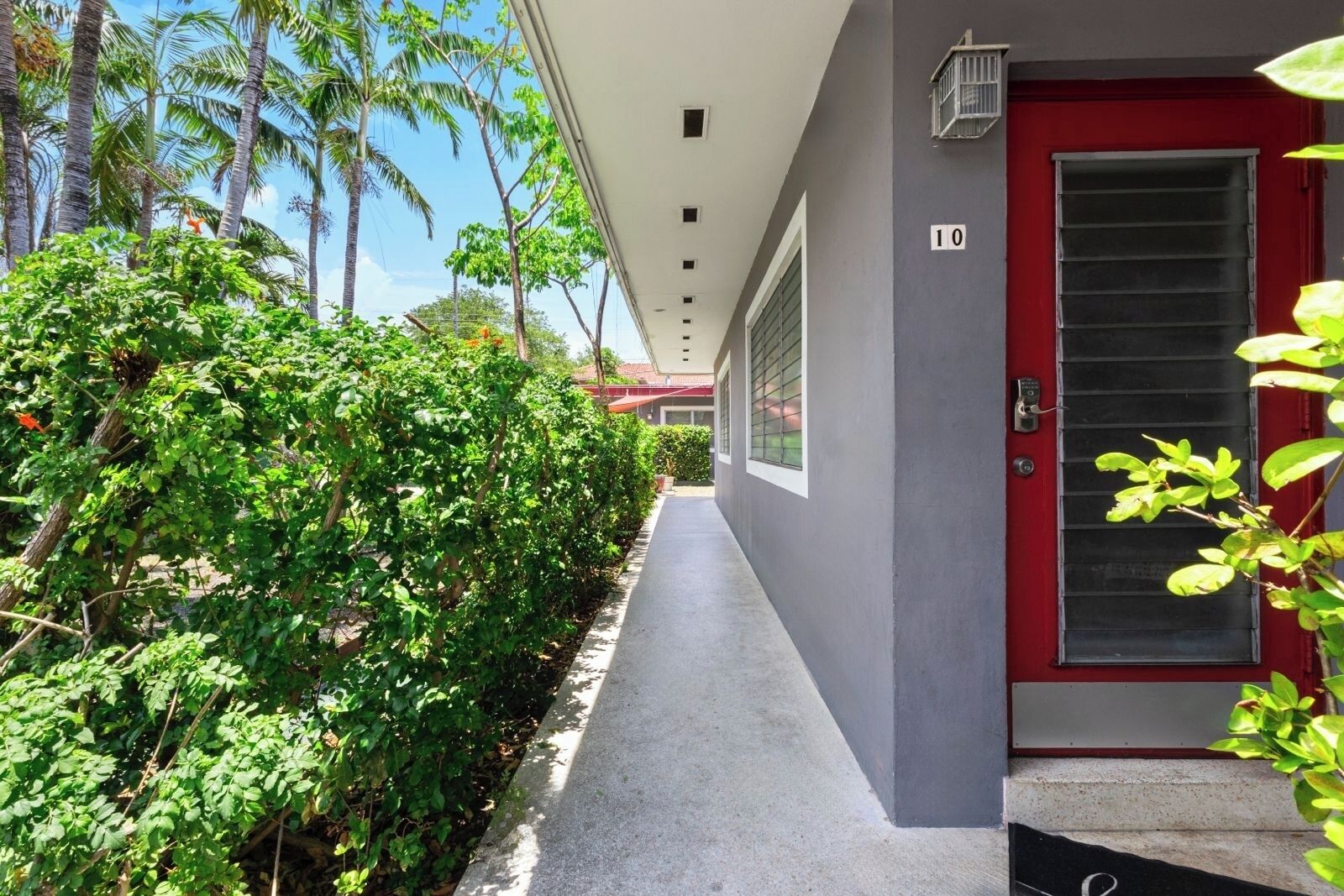A corridor with a red door marked '10', surrounded by lush greenery and palm trees.