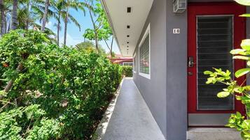 A corridor with a red door marked '10', surrounded by lush greenery and palm trees.