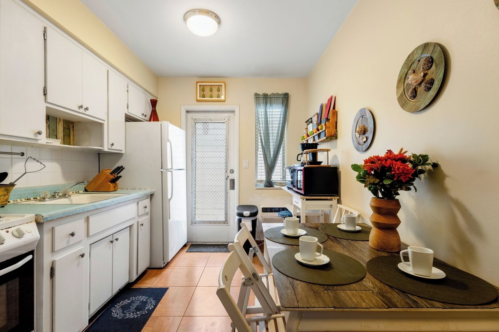 A compact kitchen with white cabinets, a stove, and a dining area with a wooden table and chairs.