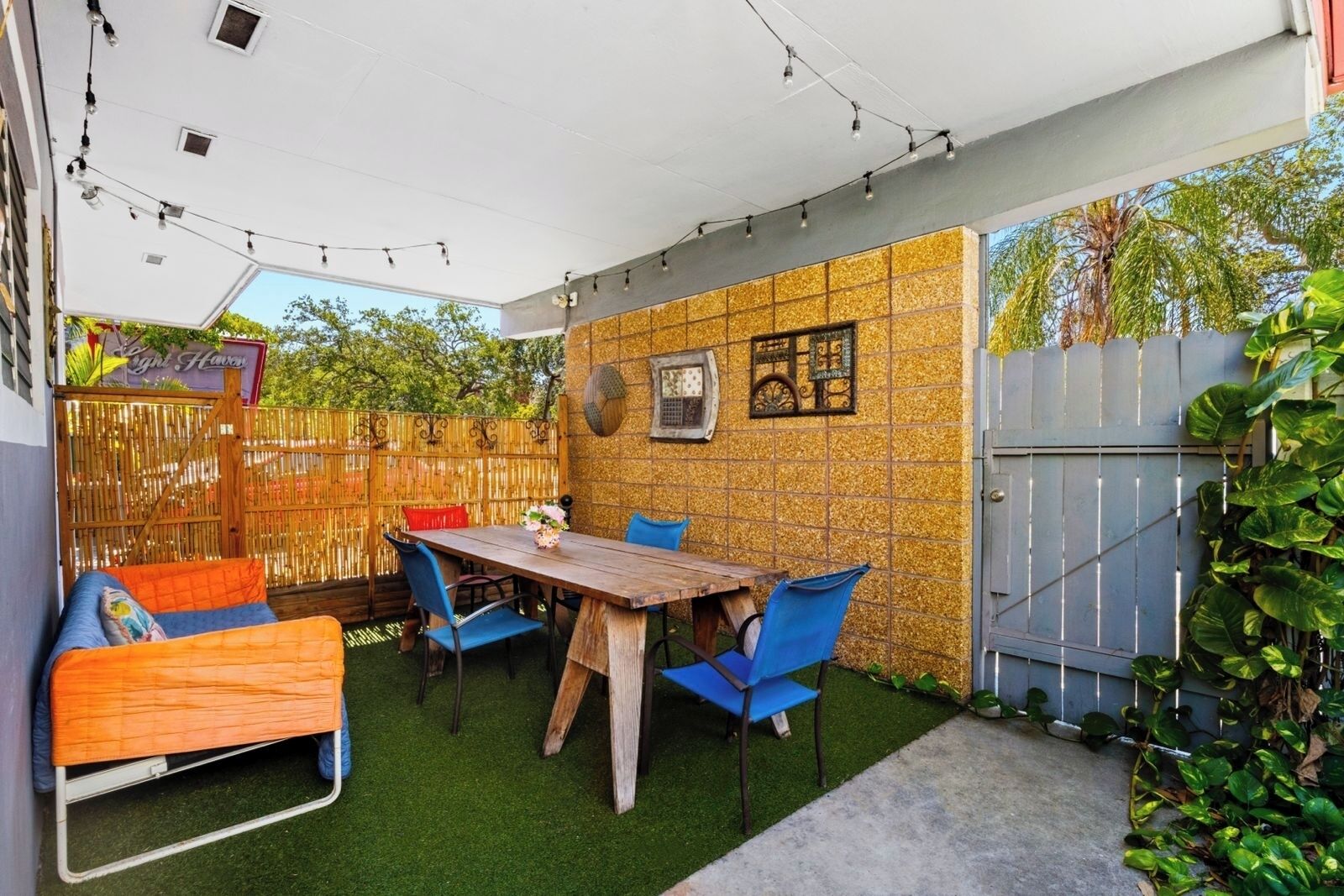 Ein Patio-Bereich mit Holztisch und blauen Stühlen, umgeben von einem Bambuszaun und einer Wand mit dekorativen Kacheln.