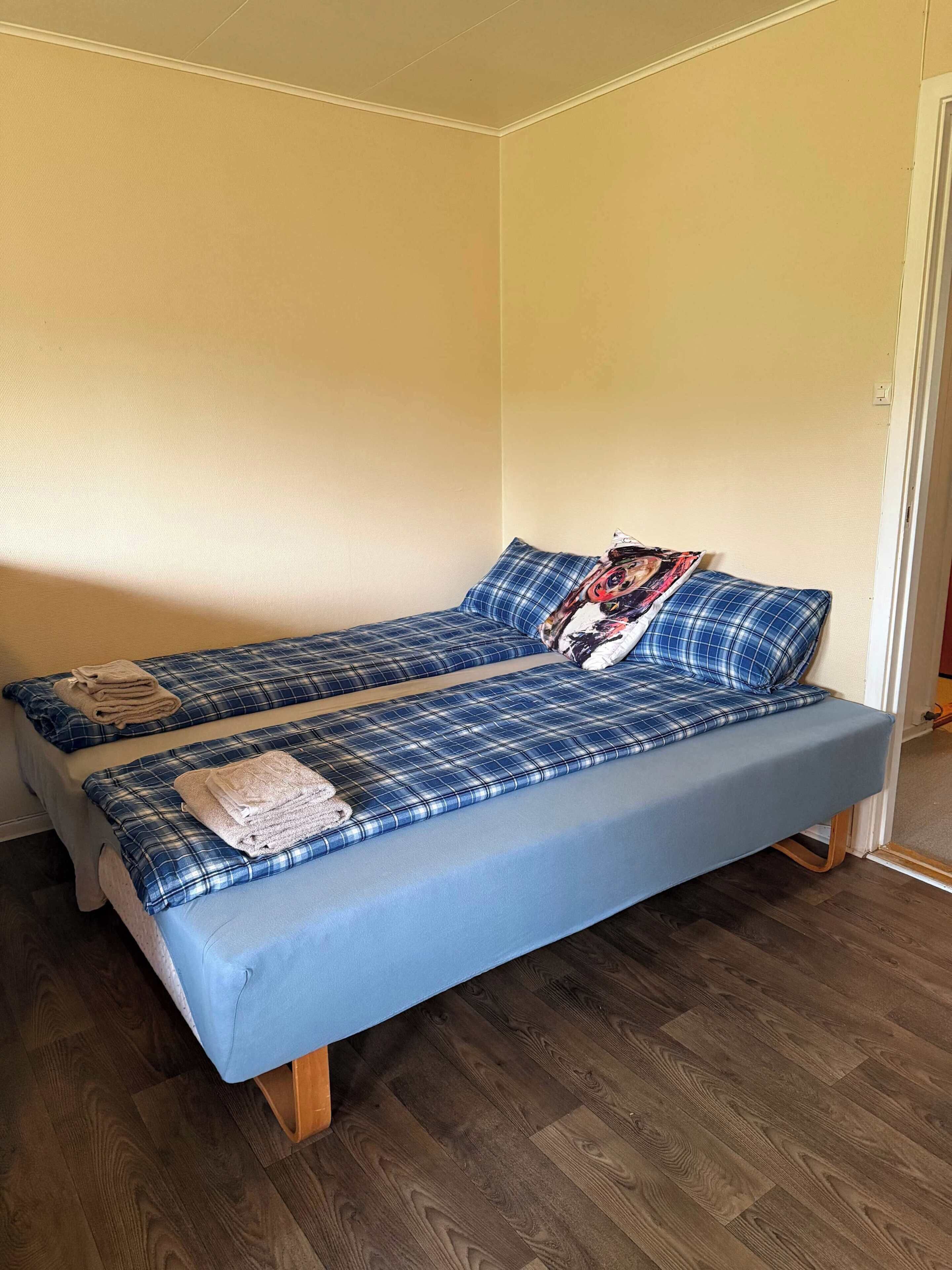 A single bed with a blue mattress and matching bedding, a pillow with a graphic design, and a folded towel on the bed.