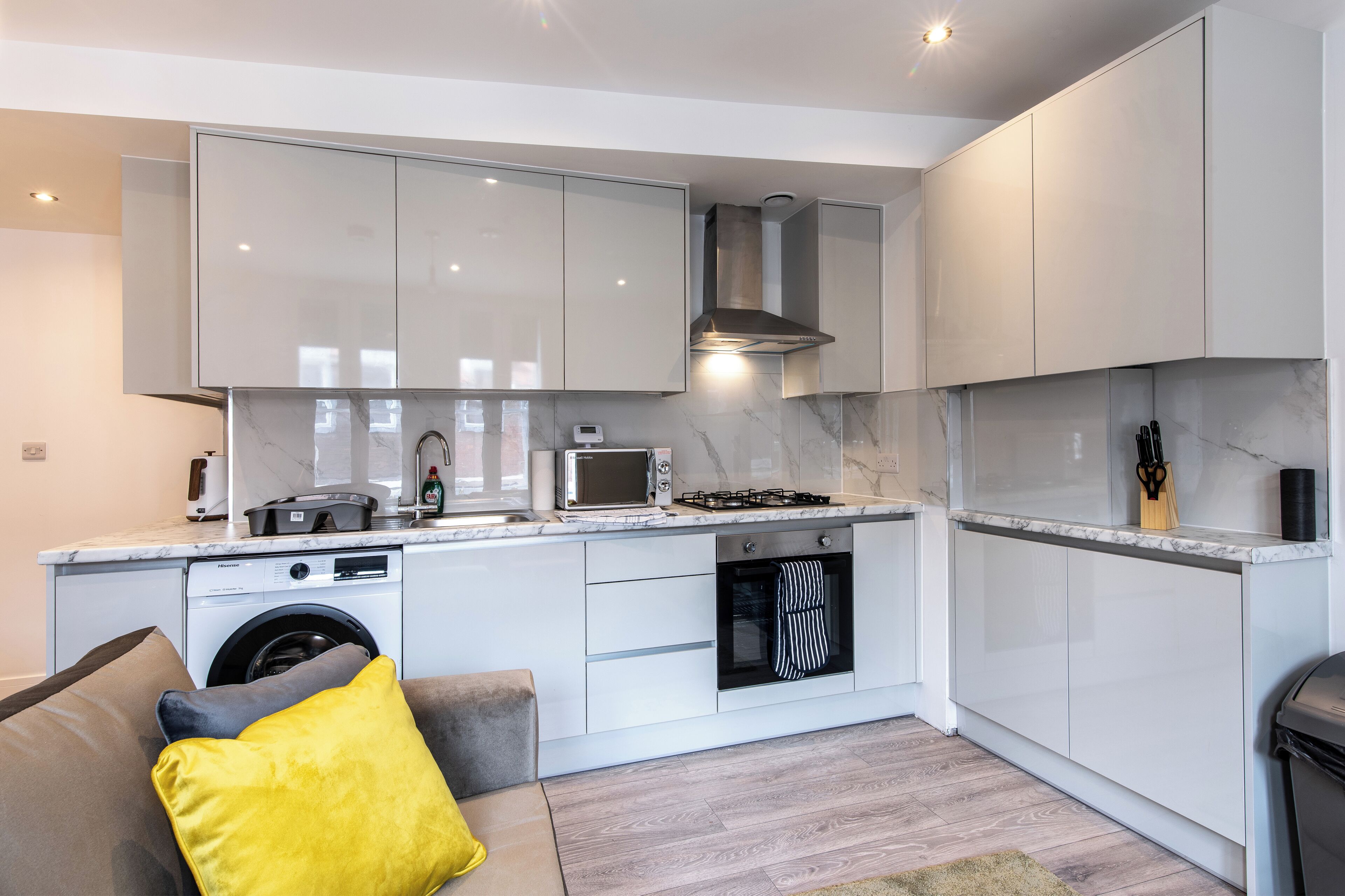 A modern kitchen with white cabinets, a built-in oven, a microwave, and a washing machine.