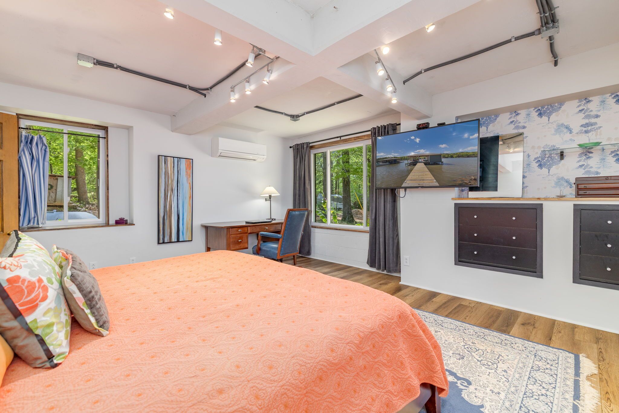 A bedroom with a bed, desk, TV, and large windows.
